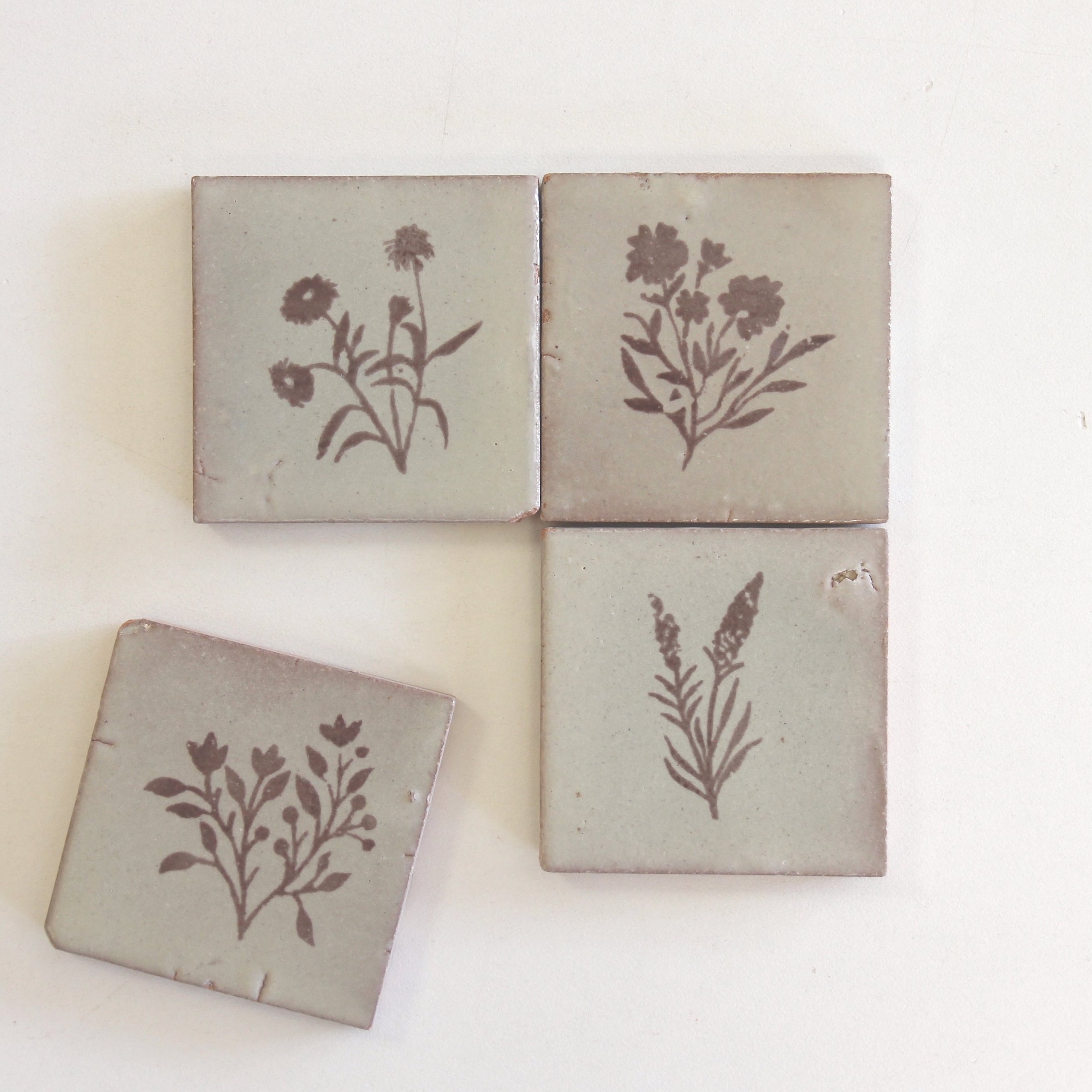 Four square tiles with floral designs on a light background