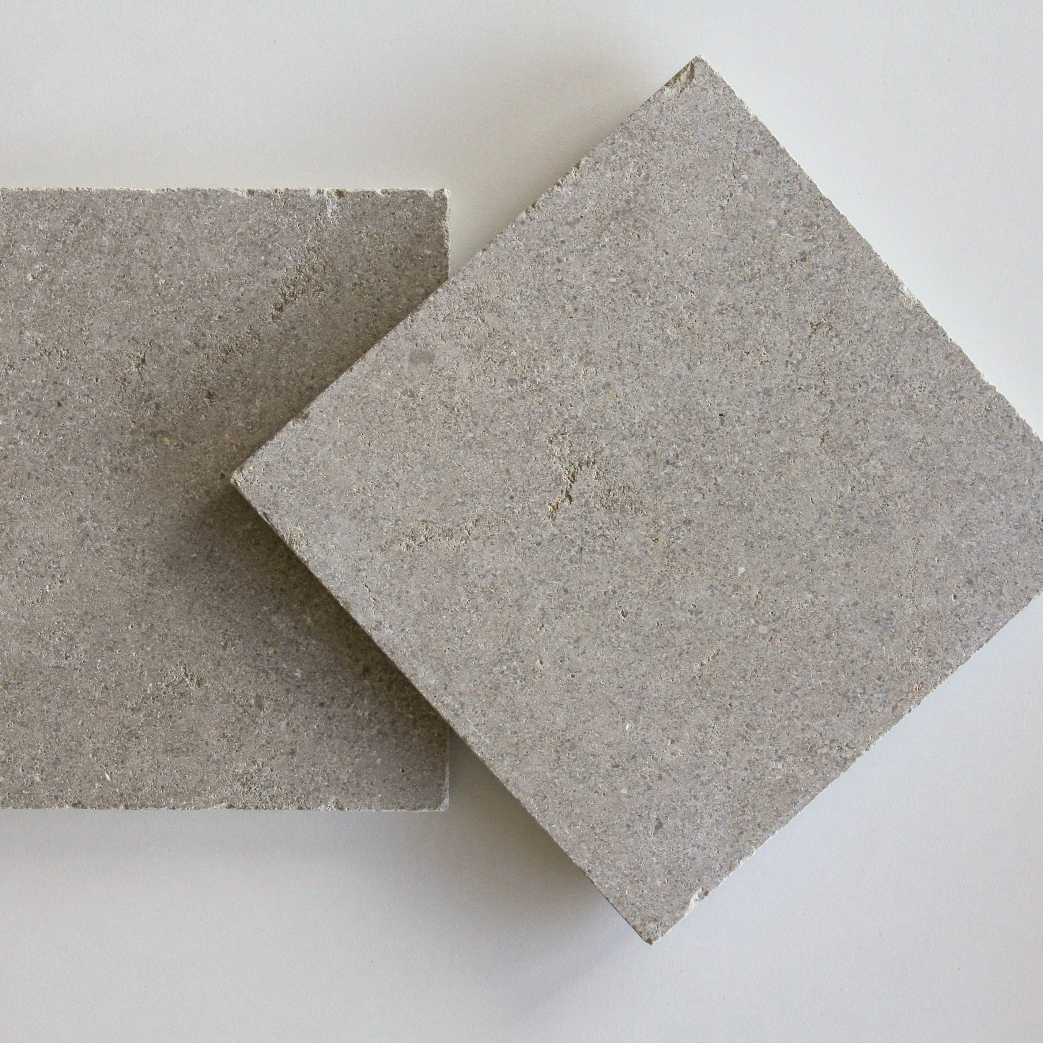 Two square tiles of Moroccan limestone, one beige and one gray, with a textured surface, placed on a white background.